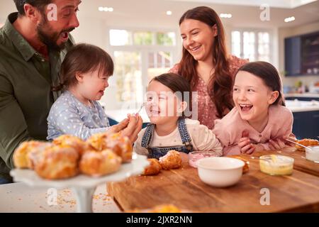 Famiglia con Down sindrome figlia cottura e decorazione torte seduti intorno al tavolo a casa Foto Stock