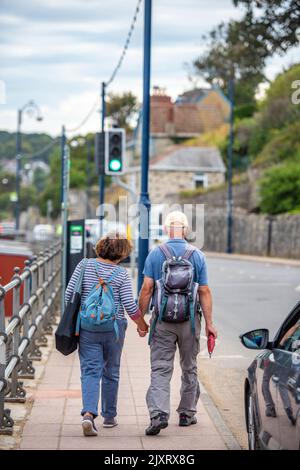 coppia di mezza età che cammina mano nella mano lungo una strada a swanage, dorset. Foto Stock
