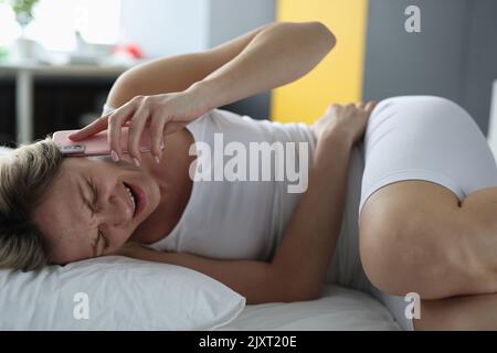 La donna malata è sdraiata a letto e parla con il medico su smartphone Foto Stock