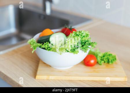 Ciotola bianca con verdure colorate pronte da mangiare lavate e mature sulla scrivania di legno in cucina. Stile di vita fermo, soft selective focus. Foto Stock