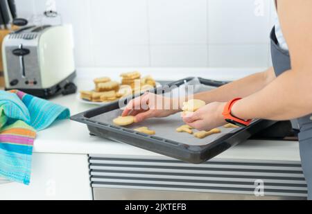 Donna che rimuove i biscotti dalla teglia da forno. Cucina casalinga. Spazio di copia. Fatti in casa. Foto Stock