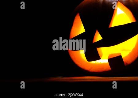 Vista ravvicinata della spaventosa zucca di Halloween con gli occhi che si illuminano all'interno su sfondo nero Foto Stock