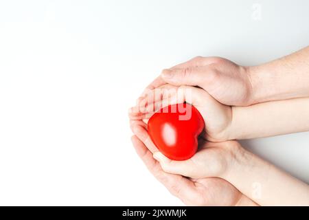 Mani dell'uomo e del bambino che tengono il cuore rosso su fondo bianco. Assistenza sanitaria, amore, donazione di organi e concetto di assicurazione familiare. Foto Stock