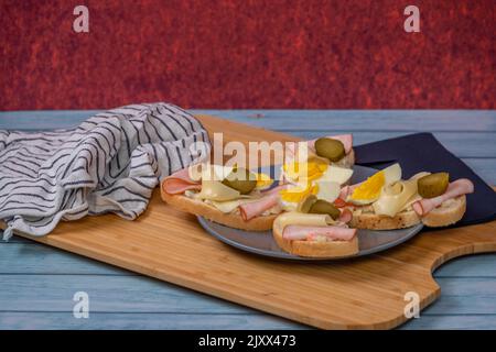 Tipico panino ceco aperto con uova, insalata di patate, prosciutto, formaggio e sottaceti su tavola di legno blu Foto Stock