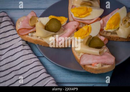 Tipico panino ceco aperto con uova, insalata di patate, prosciutto, formaggio e sottaceti su tavola di legno blu Foto Stock