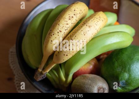 Banane macchiate di colore giallo maturo accanto alle banane verdi in un recipiente per la frutta per favorire la maturazione Foto Stock