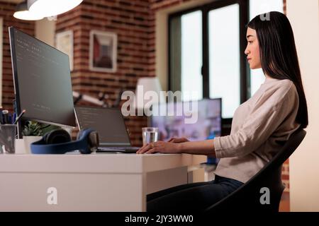 Ingegnere IT asiatico codifica app software con script html, utilizzando la crittografia del server firewall per lo sviluppo di app web. Programmatore femmina programmazione nuova interfaccia utente su più monitor. Foto Stock