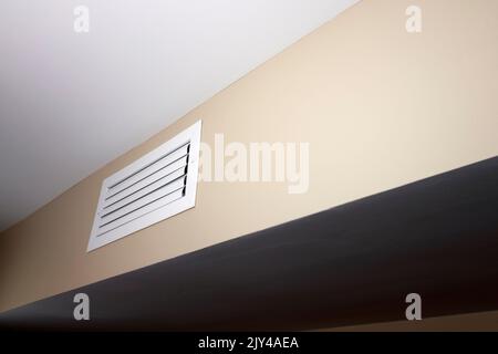 Una presa d'aria chiusa rettangolare, bianca, piccola e situata in una parete beige vicino a un soffitto bianco. Una presa d'aria chiusa rettangolare bianca all'interno Foto Stock
