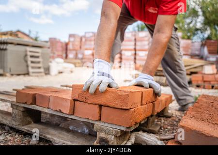 Primo piano sulle mani di uomo caucasico sconosciuto costruzione industria o magazzino di lavoro impilare mattone di argilla sulla tavolozza Foto Stock