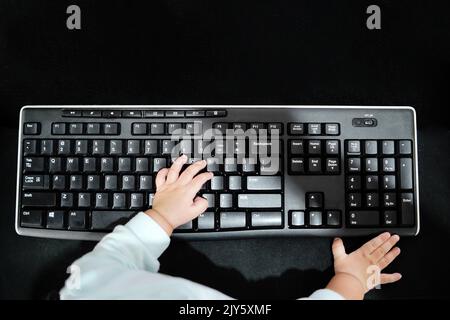 Il bambino ha le mani sulla tastiera del computer. Piccolo uomo d'affari. Esercitarsi a digitare velocemente. Stile di vita familiare Foto Stock