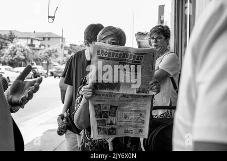 La donna legge il giornale della comunità cinese mentre fa la coda in un ristorante a Cabramatta, Sydney - nuovo Galles del Sud, Australia Foto Stock