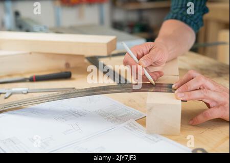 Un falegname misura tavole di legno e fa segni con una matita in un'officina. Foto Stock