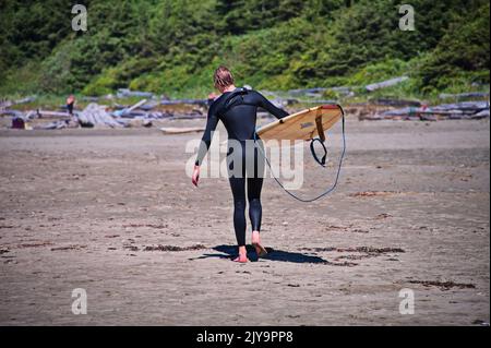 Surfista a piedi sulla spiaggia di Tofino, Canada, che porta la tavola Foto Stock