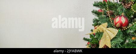 Un banner con un albero di Natale decorato con archi dorati, palline di vetro scintillante e giocattoli di albero di Natale su sfondo chiaro con una copia vuota spac Foto Stock