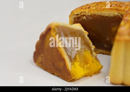 Primo piano del cuneo di torta di luna cinese tagliato con pasta di semi di loto e tuorlo d'uovo d'anatra salato, su sfondo bianco Foto Stock