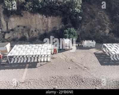 Sedie a sdraio vuote sotto un baldacchino sulla spiaggia. La spiaggia è vuota. Nessuna gente. Lettini in plastica bianca sotto il parasole. La stagione natalizia termina Foto Stock