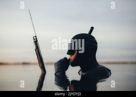 Vista laterale di un subacqueo con pistola a spruzzo mentre è immerso in acqua di mare. Giovane uomo pesca di spearfishing nel mezzo dell'oceano. Foto Stock