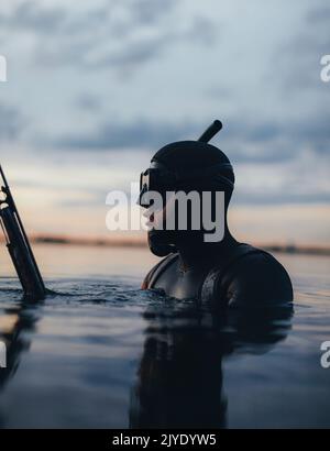 Cacciatore subacqueo pesca spearfishing in mare al tramonto. Giovane subacqueo che tiene un fucile mentre è immerso in acqua di mare. Foto Stock