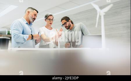 Progettisti innovativi che lavorano con 3D modelli di turbine eoliche in un ufficio moderno. Gruppo di uomini d'affari creativi che hanno una discussione mentre lavora ad un r Foto Stock