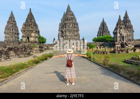 Indonesia, Prambanan- ragazza giovane con cappello in piedi con le braccia aperte guardando il tempio Prambanan durante il tramonto. Donna asiatica con vestito bianco e che indossa ha Foto Stock