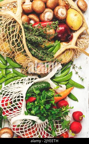 Selezione di cibi sani: Funghi, fagioli, pomodori, avocado ed erbe. Sacchetti riutilizzabili in tessuto per lo shopping pieni di verdure primaverili biologiche provenienti dalla zona Foto Stock