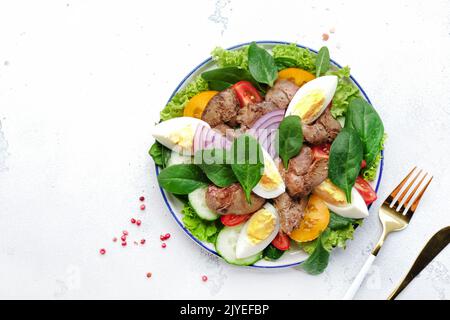 Insalata di perigord con fegato di pollo, pomodori, cetrioli, uova, lattuga e spinaci. Sfondo bianco tavolo da cucina, vista dall'alto Foto Stock