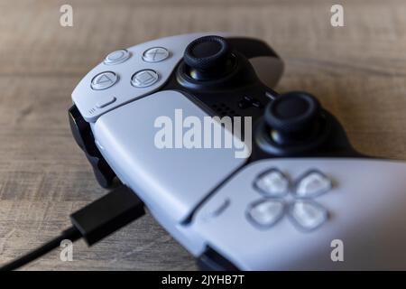 BRECHT, BELGIO – AGOSTO 14 2022: Ritratto di un controller base playstation 5 bianco che si ricarica con il cavo USB-C ufficiale situato in interni o Foto Stock