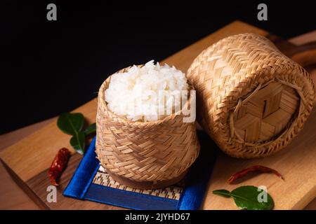 Asian Food Concept riso glutinoso o riso Sticky in vimini di bambù su tavola di legno e sfondo nero con spazio copia Foto Stock