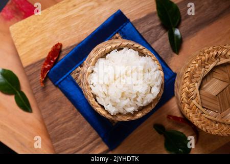 Asian Food Concept riso glutinoso o riso Sticky in vimini di bambù su tavola di legno e sfondo nero con spazio copia Foto Stock