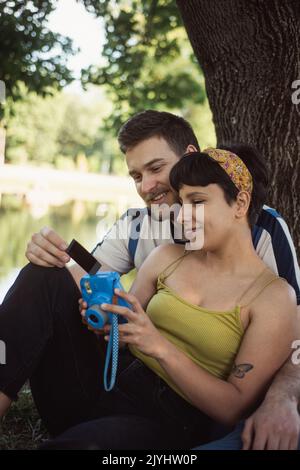 Coppia incredibile guardando la foto mentre si siede sull'erba vicino all'albero nel parco Foto Stock