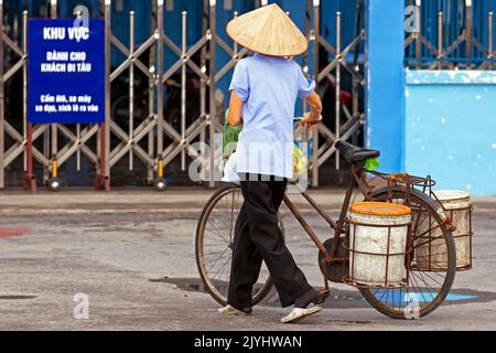 Signora vietnamita che indossa un cappello di bambù andare in traghetto con biciclette che trasportano merci, Hai Phong, Vietnam Foto Stock