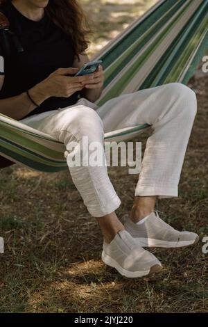 Uomo con smartphone seduto sull'amaca Foto Stock