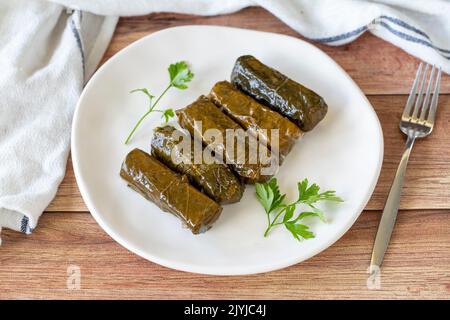 Foglie avvolte con olio d'oliva su fondo ligneo. Specialità della cucina mediterranea tradizionale. Nome locale zeytinyagli yaprak sarma o dolmadika. Foto Stock