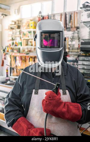 Lavorazione del metallo con un uomo che utilizza una saldatrice per la cucitura dell'acciaio. Fabbro in abiti speciali, casco e guanti per lavori di lavorazione dei metalli Foto Stock