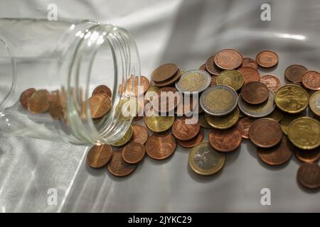 alcune monete in euro che si riversano dal vaso di vetro per pagare le fatture Foto Stock