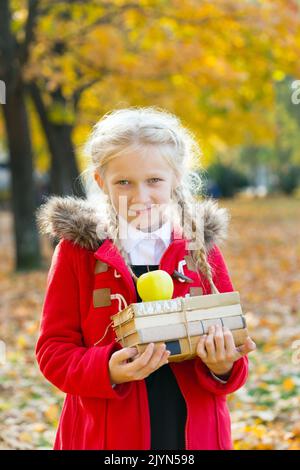 Sorridente schoolgirl può contenere libri e Apple nelle sue mani nel parco su una caduta al giorno. Passeggiata d'autunno Foto Stock