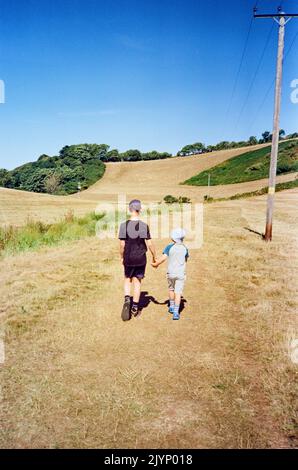 Fratelli Holing mani che camminano attraverso un campo, Hope Cove, Kingsbridge, South Devon, Inghilterra, Regno Unito. Foto Stock