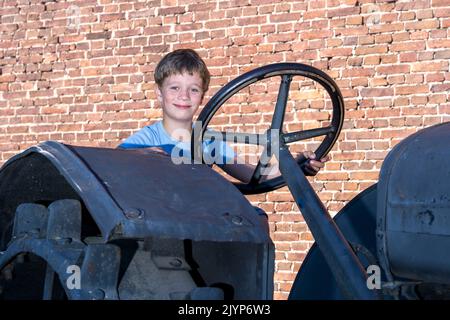 un ragazzo che guida un vecchio trattore d'epoca sullo sfondo di un muro di mattoni Foto Stock