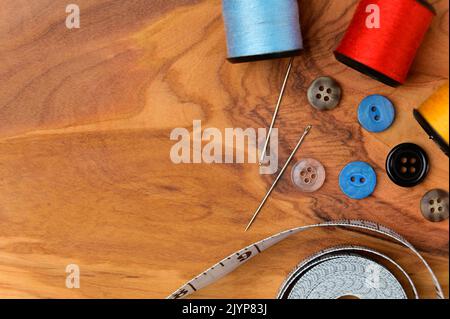 Accessori per cucire e tessuto su fondo legno. Fili, aghi, tessuto, bottoni e metro a nastro. Vista dall'alto. Foto Stock