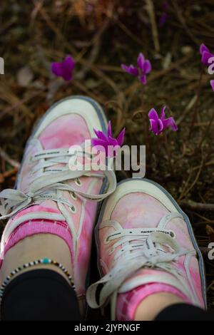 Madrid, Spagna. Settembre 6, 2022 ragazza elegante in sneakers rosa seduta tra viola ciclamino hederifolium fiori sul bordo della foresta, giardino, parco. Foto Stock