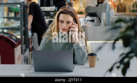 Donna d'affari seria studente manager freelance seduto a un tavolo con laptop che risponde a una chiamata parlando al telefono arrabbiato discutere con i colleghi Foto Stock