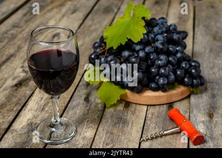 Bicchiere di vino con vino rosso, cavatappi e uva fresca su tavola di legno. Messa a fuoco selettiva. Foto Stock