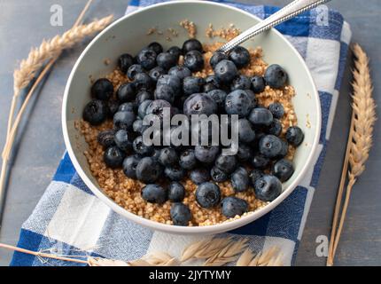 Colazione porridge di cereali con avena, amaranto, quinoa e mirtilli freschi in una ciotola con cucchiaio Foto Stock