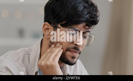 Primo piano malato uomo indiano in occhiali maschio triste ispanico arabo barbuto uomo sofferente dolore dentale. Il tipo ritratto sente il disagio di mal di denti in carie gengivali Foto Stock
