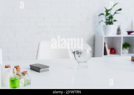 KIEV, UCRAINA - 29 GIUGNO 2022: Sfera di cristallo vicino a tar card e bottiglie con oli essenziali su tavolo bianco Foto Stock