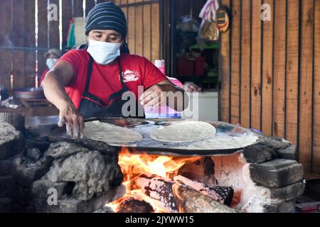 Donna che cucina Tlayudas su un fuoco di legna, Oaxaca México Foto Stock