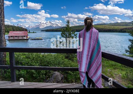 Donna coccolata in una coperta rosa gode della vista del lago Maligne nel Jasper National Park durante l'estate Foto Stock