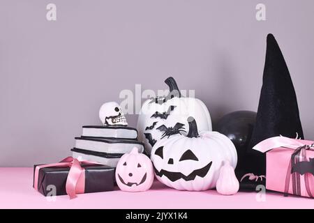 Decorazioni di Halloween rosa e bianco con zucche bianche e nere, cappello di strega e libri di magia su sfondo grigio Foto Stock