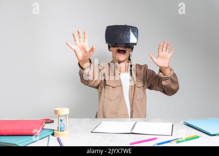 Bambino che studia con gli occhiali vr per i compiti e le lezioni online alla scrivania. Giovane ragazza con cuffie che si prepara per corsi e lezioni a distanza Foto Stock