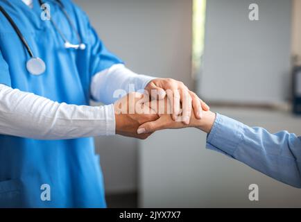 Medico maschile giovane in uniforme calmante, scuotendo la mano con la vecchia paziente in clinica Foto Stock